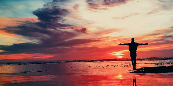 Silhouette of person with outstretched arms next to the ocean